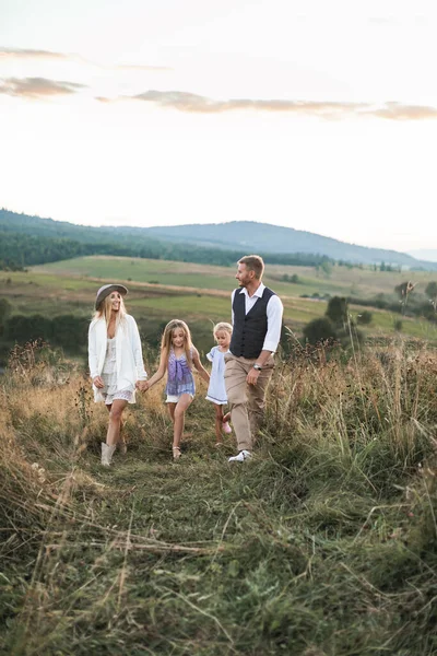 Família feliz, pai, mãe, e duas meninas bonitos em casual boho desgaste andando juntos no campo ao pôr do sol. O conceito de harmonia, família e amor, felicidade e alegria — Fotografia de Stock