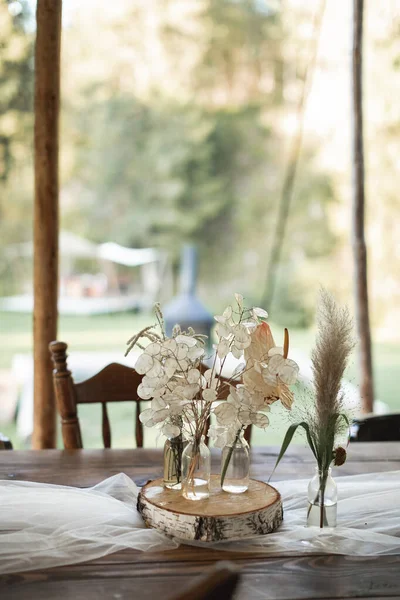 Decorações de mesa rústicas ao ar livre. Bouquets de flores, flores silvestres secas em frascos de vidro em uma banheira de madeira deitada em uma mesa de madeira festiva, casamento ou mesa de jantar ao ar livre — Fotografia de Stock