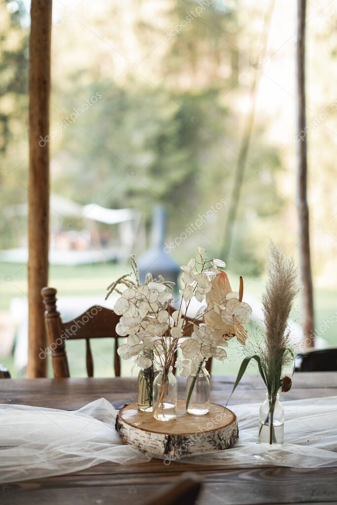 Decorazioni da tavolo rustiche all'aperto. Mazzi di fiori, fiori selvatici  secchi in vasi di vetro su una vasca di legno sdraiato su un tavolo di legno  festivo, matrimonio o cena all'aperto 