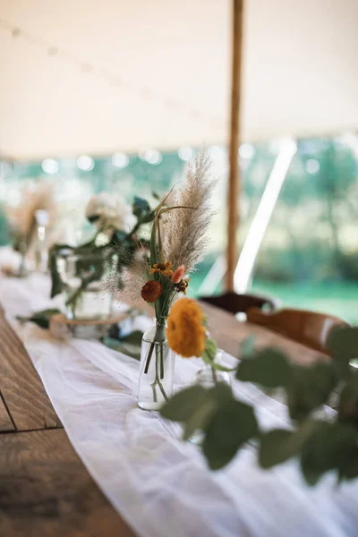 Decorações de mesa rústicas ao ar livre. Bouquets de flores, flores silvestres secas em frascos de vidro em uma banheira de madeira deitada em uma mesa de madeira festiva, casamento ou mesa de jantar ao ar livre — Fotografia de Stock