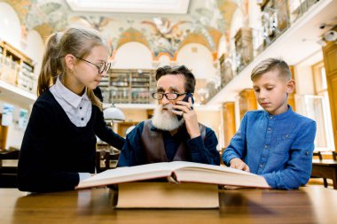 Zeki, yaşlı, sakallı bir adam telefonda konuşuyor. Genç torunu ve torunuyla hoş vakit geçiriyor. Kütüphanede ilginç bir kitap okuyor.