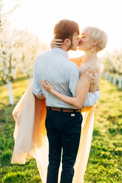 Joyeux baiser couple de mariage amoureux dans un beau jardin fleuri au printemps jour ensoleillé, homme tenant femme sur les mains. Embrasser couple dans le jardin fleuri au printemps — Photo