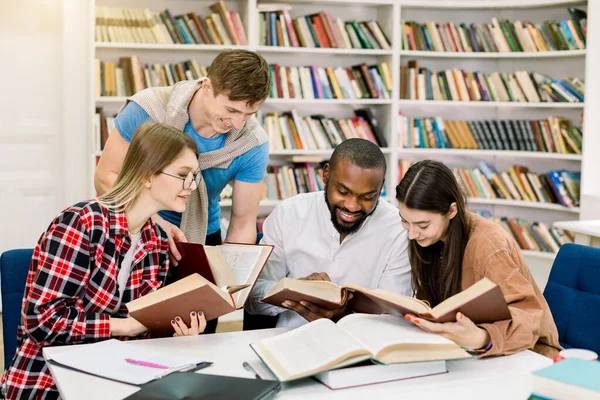 Jóvenes multirraciales disfrutando del estudio en grupo en la mesa de la biblioteca. Estudiantes universitarios felices sentados juntos en la mesa con libros y laptop para investigar información para su proyecto o exámenes —  Fotos de Stock