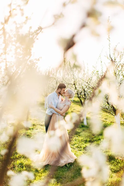 Joyeux couple sensuel amoureux embrassant et embrassant, profitant d'un moment dans le jardin en fleurs. Amour au printemps, vue à travers les arbres en fleurs — Photo