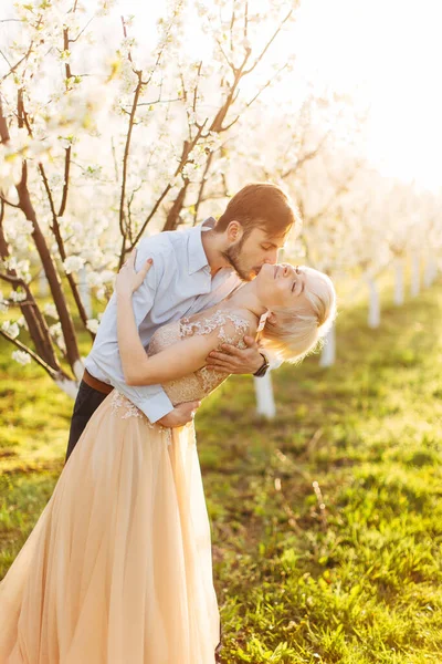 Casal bonito, alegre e romântico no amor posando no jardim florescente. Bonito homem beijando pescoço de sua mulher bonita em vestido elegante com grande paixão e amor. Retrato de casamento primavera — Fotografia de Stock