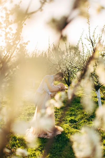 Charmant couple affectueux et tendre marchant dans un jardin fleuri au lever du soleil. L'homme serre et tient sa femme dans ses bras. Histoire d'amour, concept de mariage, rendez-vous romantique dans la nature . — Photo