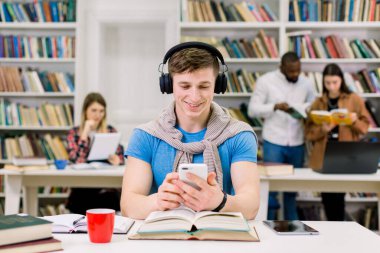 Kütüphanedeki masada oturan komik gülümseyen genç adamın portresi, telefon çalma listesindeki favori melodilerin tadını çıkarması, sınav hazırlıkları sırasında ara vermesi. Öğrenci hayatı konsepti