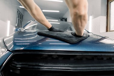 Araba temizleme konsepti. Siyah mikrofiberi tutan ve arabanın kaputunu cilalayan profesyonel erkek oto yıkama işçisinin elleri. Aşağıdan görüntüle