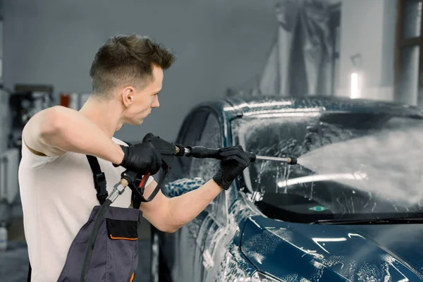 Araba yıkamada yüksek basınçlı suyla modern mavi otomobili temizleyen bir işçinin yan bakışı. Araba yıkama ve detay verme konsepti — Stok fotoğraf