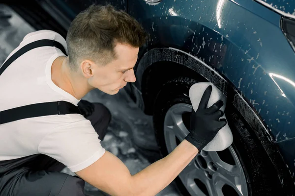 Bir arabayı elle yıkamak. Modern mavi arabanın çarkını yıkayan genç adamın araba yıkama servisinde süngerle üst açılı görüntüsü. — Stok fotoğraf