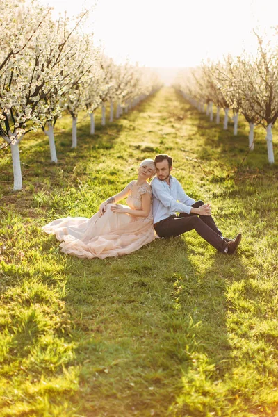 Plan lumineux de jeune couple relaxant au printemps jardin fleuri sur l'herbe verte, assis dos à dos, chacun regardant vers l'air avec un sourire réfléchi et des sentiments d'amour — Photo