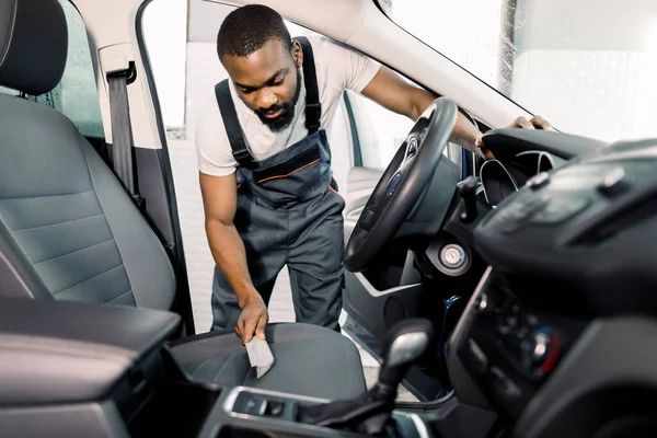 Hombre africano, trabajador profesional del servicio de lavado de coches, hace una limpieza de cepillo de asiento de coche. Limpieza completa de todas las partes de un coche, limpieza en seco, servicio profesional, detalles del coche — Foto de Stock