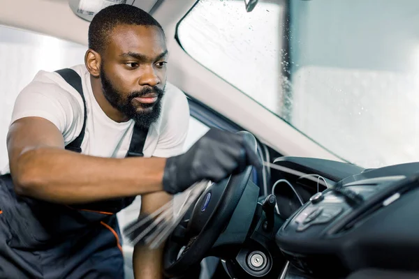 Homem africano, trabalhador de serviço de carro profissional em luvas de proteção preto, limpeza interior do carro com escovas especiais. Auto detalhamento e valeting conceito — Fotografia de Stock