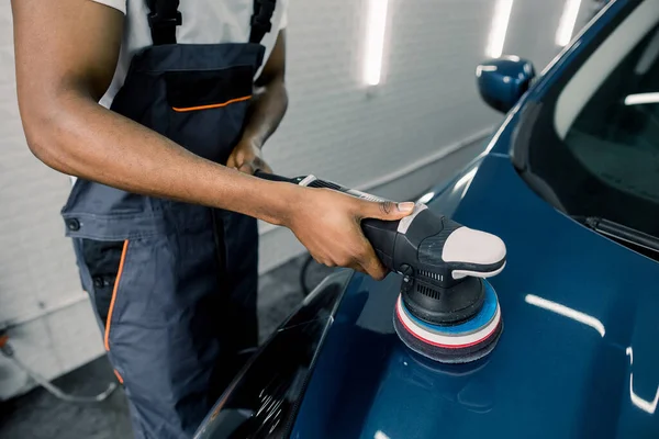 Bilpoleringsprocess. Beskuren bild av händer mörkhyade bilservice anställd i arbetsoverall, polering blå bilhuva med polermaskin, keramisk beläggning — Stockfoto