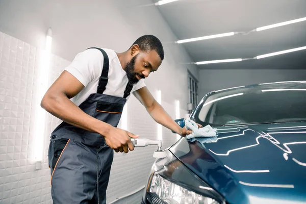 Hombre africano coche profesional detallando trabajador, pule un coche azul con un pulidor y tela de microfibra. Concepto de detalle del coche — Foto de Stock