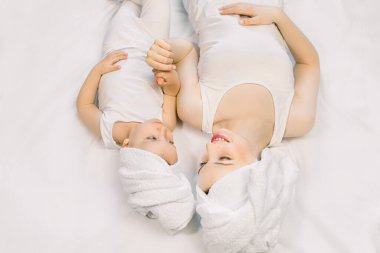 Genç anne küçük kızıyla evde yatakta oynuyor. Anne ve tatlı kız kafalarında beyaz havlularla banyodan ve spa ameliyatlarından sonra izole edilmiş arka planda birlikte yatıyorlar. Mutlu aile, anneler günü