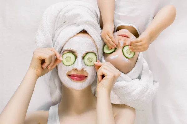 Maman et sa petite fille de 2 ans s'amusent ensemble, faisant un masque facial en argile et des tranches de concombre sur les yeux. Mère avec un enfant faisant un traitement de beauté ensemble. Temps en famille, spa et beauté, fête des mères — Photo