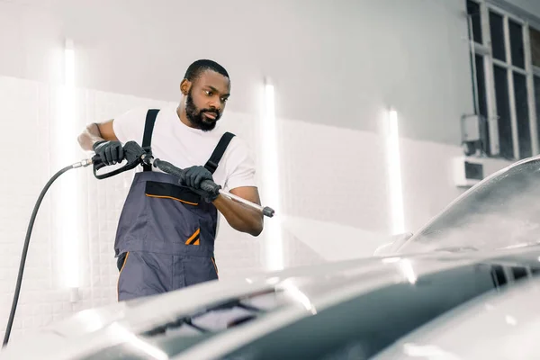 고압 물총을 사용하여 차를 닦는 일. 직업적 인 자동차 세차장에서 고압 의물 속에서 현대식 고급 승용차를 씻고 있는 아프리카 계 미국인 청년 — 스톡 사진