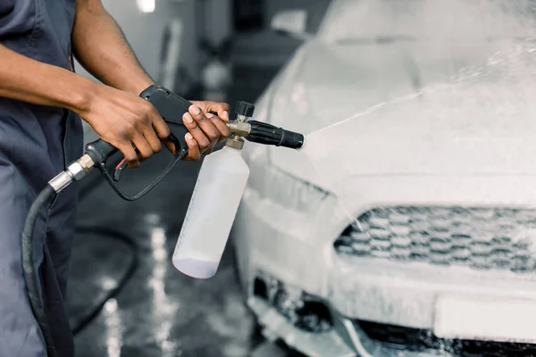 Conceito de lavagem de carro manual. Imagem cortada de mãos de jovem trabalhador de pele escura limpando carro branco moderno com espuma e água pressurizada na estação de serviço. Manual detalhando lavagem de carro — Fotografia de Stock