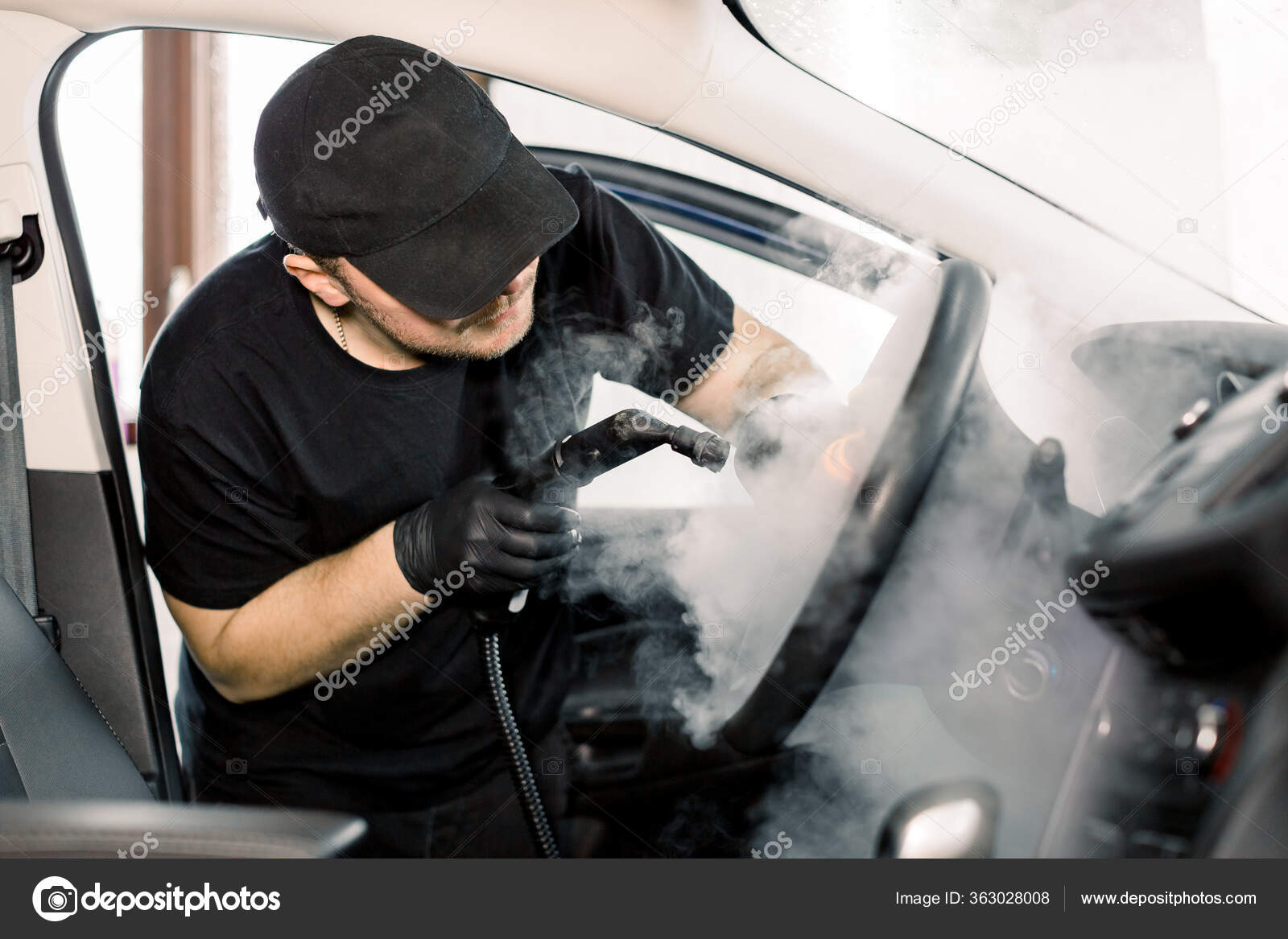 Fotos de Detallado de coches, concepto de limpieza de vapor. Hombre guapo  en camiseta negra y gorra, trabajador del centro de lavado de coches,  limpieza interior del coche con limpiador de vapor