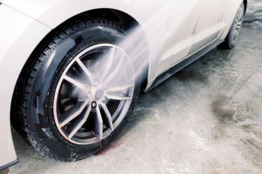 Temizlik servisinde araba yıkamak. Arabanın tekerleklerini yüksek basınçlı su tabancasıyla yıkama işleminin görüntüsünü özel kırmızı temizleyici solüsyonla temizledikten sonra kapat