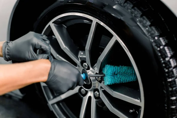 Servicio de lavado automático. Imagen de cerca recortada de manos masculinas en guantes protectores negros, llantas de limpieza de aleación llantas de coche de lujo con un cepillo especial para ruedas fundidas en un taller de detalles del vehículo — Foto de Stock