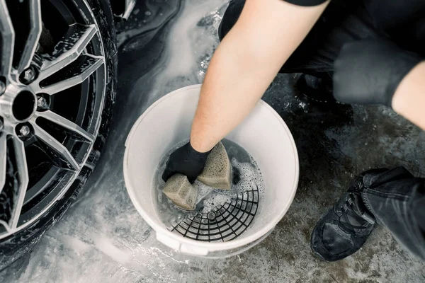 Biltvätt och detaljerat koncept. Ovanifrån av tvättverktyg i biltvätt service, vit hink med tvål rengöringslösning, speciell grill. Hand manlig arbetare som håller svamp för rengöring av bilfälgar — Stockfoto