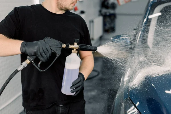 Biltvätt med rinnande vatten och skum. Sidovy över unga biltvätt service manliga anställd håller högtrycksspray med rengöringsskum. Biltvätt. Tvättmaskin på stationen — Stockfoto