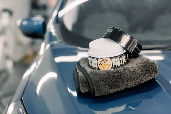 Araba temizliği ve cilalama konsepti. Araba cilalamak, cilalamak, mikrofiber bez, Carnauba cilası, lüks mavi arabanın kaputunda uzanmak, araba tamirhanesinde