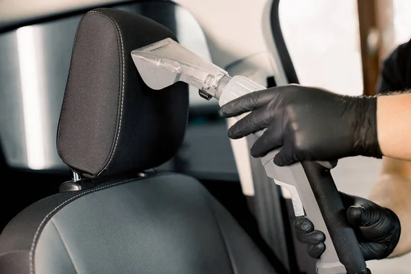 Cropped image of hands of car service worker, wearing black protective gloves, cleaning car front seat with wet vacuum cleaner. Car wet chemical vacuum cleaning, car detailing concept — Stock Photo, Image