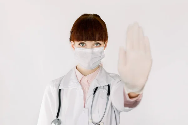 Covid19, коронавірус, медична допомога та медична концепція. Серйозний кавказський лікар у медичній масці, з стетоскопом і білим пальтом, показує знак "Стоп" рукою в захисній рукавичці. — стокове фото