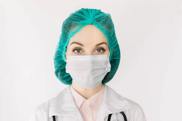 Медицина та медичне обслуговування. Заверніть портрет кавказької жінки - лікаря, медсестри, лаборанта або вченого у захисній масці, зеленій шапці та білому пальто на білому тлі. — стокове фото