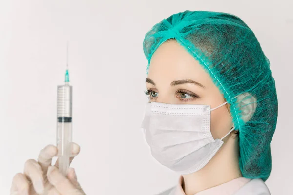 Молода жінка медсестра або лікар в білому лабораторному пальто, шапка і маска, з шприцом в руках, готує шприц для вакцинації, ізольовані на білому тлі. Медична та медична концепція — стокове фото