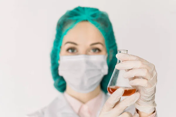 Концепція охорони здоров'я та медицини, COVID-19 . Серйозна жінка-лікар вірусолог тримає в руках скляну хімічну колбу з червоною рідиною. Розробка нових ліків або вакцин. Фокус на колбі в руках — стокове фото