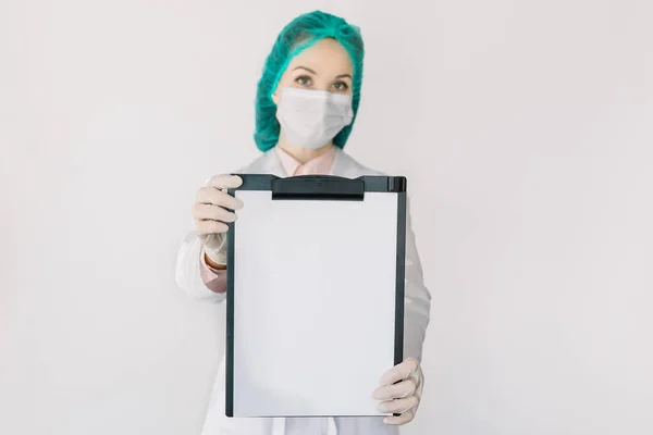 Медична жінка-спеціалістка, лікар або медсестра, носить медичну шапочку та маску, показуючи буфер обміну з чистим папером на камеру, ізольовані на білому, копіюють простір. Медицина, лікар, охорона здоров'я — стокове фото