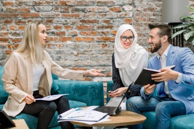 Üç iş adamından oluşan yaratıcı bir grup, Kafkas erkek ve kadın, Müslüman kadın, beyin fırtınası yapan ve gülen, proje mali raporları ve dizüstü bilgisayarla çalışan, ofisteki koltukta oturan