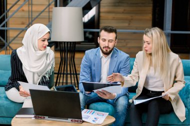 Yakışıklı, sakallı, beyaz iş adamı ve birbirine danışan iki çok ırklı iş kadını modern çatı katında ortak finansal proje üzerinde çalışıyorlar.