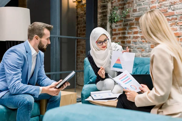 Jolie femme d'affaires musulmane, leader du projet, parlant avec ses deux collègues caucasiens, homme et femme, remue-méninges, discuter du plan d'affaires, lors de la réunion au bureau moderne — Photo