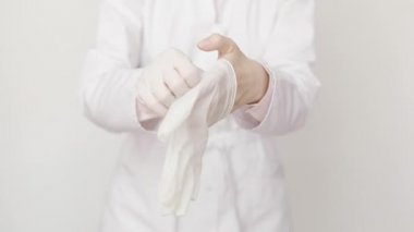 Beyaz önlüklü kadın doktor ya da hemşire beyaz koruyucu lastik eldiven giyiyor. Yakın çekim, beyaz arka planda izole edilmiş. Sağlık ve ilaç, hijyen ve hastalık önleme kavramı