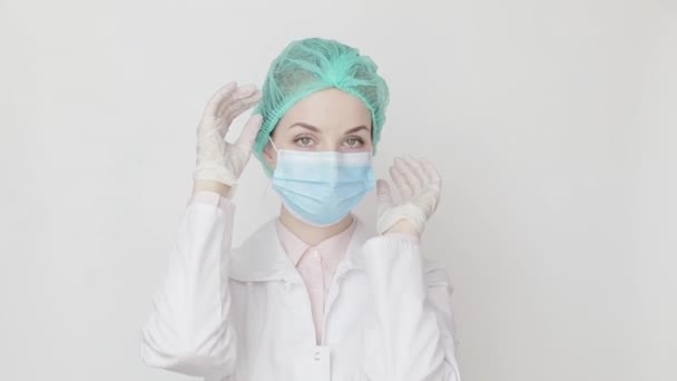 Ritratto di giovane dottoressa o infermiera caucasica vestita con berretto medico e maschera facciale che guarda la macchina fotografica su sfondo bianco. Concetto di prevenzione sanitaria, medica e delle malattie . — Video Stock