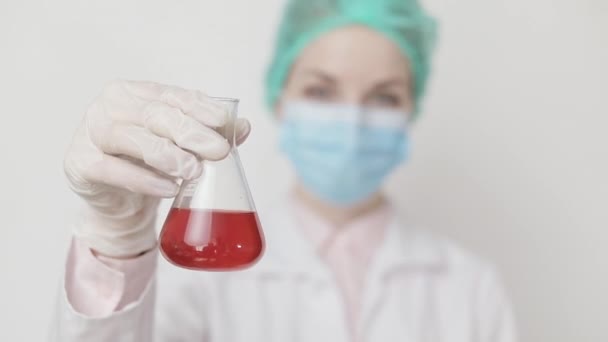 Zbliżenie młodego chemika, lekarza, naukowca patrzącego na płyn w szklanej kolbie w laboratorium, potrząsającego kolbą. Kobieta chemik analizujący płyn chemiczny w kolbie. Nauka, medycyna, biotechnologia — Wideo stockowe