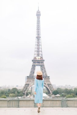 Mavi elbiseli ve şapkalı şık turist kadının Paris, Fransa 'da Eyfel Kulesi' ni gezerken arkadan görünüşü
