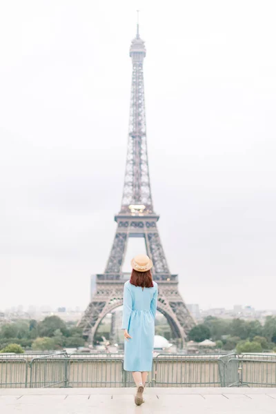 Rückansicht einer stilvollen Touristin in blauem Kleid und Hut, die den Eiffelturm in Paris besichtigt — Stockfoto