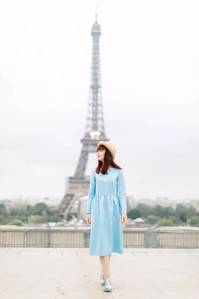 Retrato de uma jovem francesa romântica em chapéu elegante e vestido azul na moda em frente à torre Eiffel em Paris, caminhando e olhando para — Fotografia de Stock