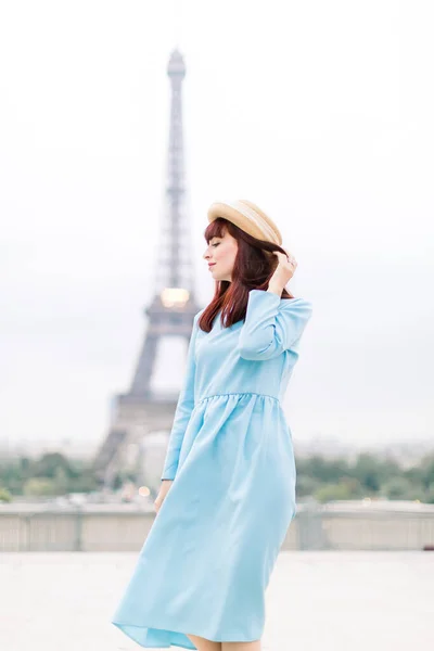 Menina bonita vestindo vestido azul longo e chapéu de palha, posando e aproveitando o momento em Paris com a torre Eiffel no fundo . — Fotografia de Stock