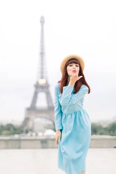 Torre Eiffel di Parigi. Bella donna caucasica in cappello e vestito blu, sorridente felice e rendendo bacio d'aria al punto di vista Trocadero di fronte alla Torre Eiffel a Parigi, Francia — Foto Stock