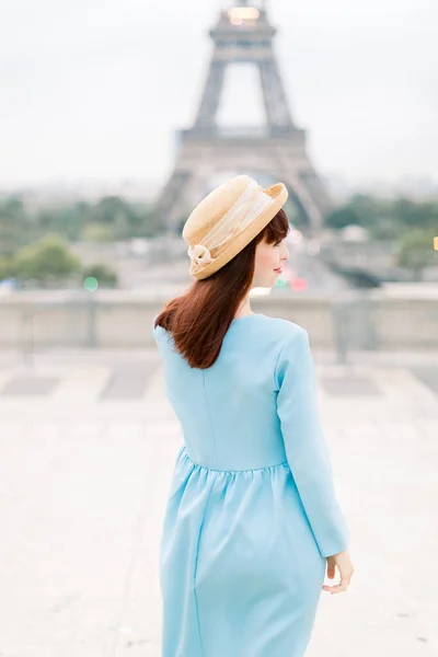 Bella ragazza in stile moda a Parigi. Giovane donna felice sorridente che cammina in cappello e vestito blu davanti alla Torre Eiffel, Parigi, Francia . — Foto Stock