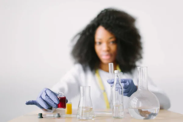 Молодая красивая афроамериканка-врач в белом халате со стетоскопом. сидя за столом с реагентными колбами на белом фоне. Женщина лаборантка с анализом крови на СПИД — стоковое фото
