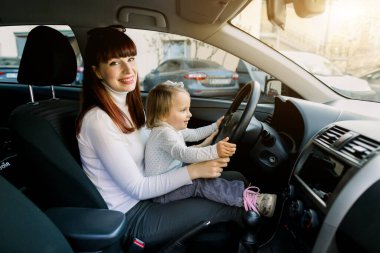 Küçük kızıyla genç bir anne arabanın ön koltuğunda direksiyonun yanında oturuyor. Araba kullanıyormuş gibi davranan bir kadın ve bebek. Anne bebeğine içerideki arabayı gösterir.