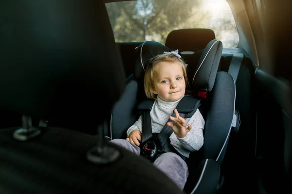 Criança branca bonito, menina bonita, sentado em assento de segurança dentro do carro com cintos apertados. Prevenção de perigos, transporte de segurança infantil — Fotografia de Stock